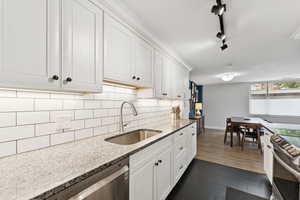 Kitchen with stainless steel appliances, white cabinets, decorative backsplash,  stone counters, and  tile floors