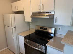 Kitchen featuring electric stove, under cabinet range hood, light countertops, white cabinets, and freestanding refrigerator