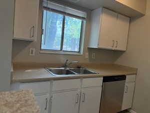 Kitchen with stainless steel dishwasher, white cabinetry, and light countertops