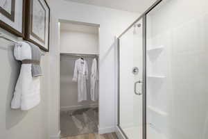 Bathroom with a spacious closet, a shower stall, and wood finished floors
