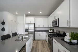 Kitchen with appliances with stainless steel finishes, light wood-type flooring, recessed lighting, white cabinetry, and a textured ceiling