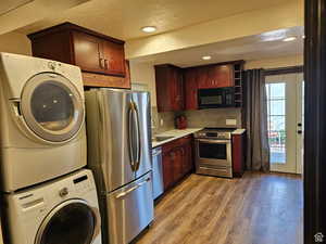 Kitchen with stainless steel appliances, stacked washing machine and dryer, light wood finished floors, a textured ceiling, and light countertops
