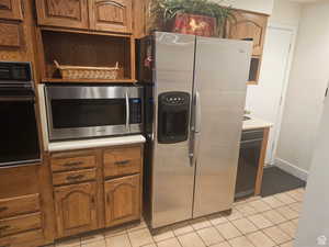 Kitchen featuring stainless steel appliances, brown cabinets, light tile patterned floors, and light countertops