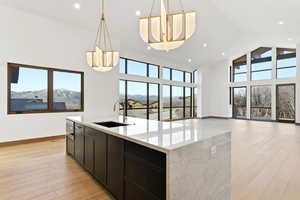 Kitchen featuring light wood-style floors, open floor plan, light stone counters, an island with sink, and a high ceiling