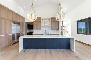 Kitchen featuring light stone countertops, pendant lighting, stainless steel built in fridge, vaulted ceiling, and light wood-style flooring