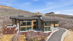 Back of property with stone siding, a shingled roof, a chimney, and a sunroom
