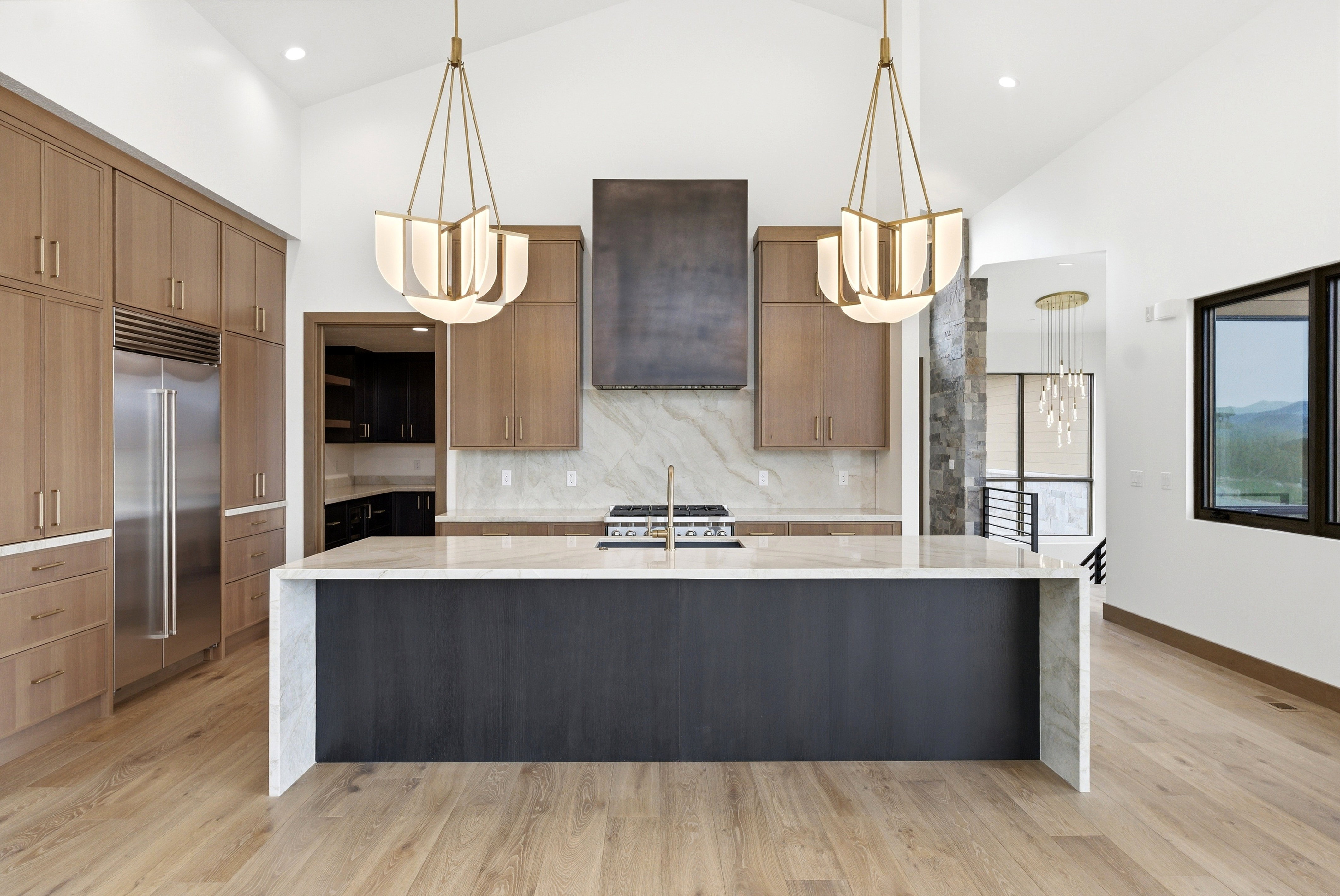Open-concept kitchen featuring a large central island with a waterfall countertop, integrated stainless steel refrigerator, and wood-finish flooring