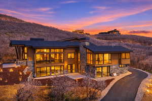 Back of house at dusk featuring stone siding, a chimney, and driveway