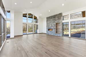 Unfurnished living room with a high ceiling, a stone fireplace, healthy amount of natural light, light wood finished floors, and recessed lighting