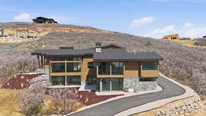View of front facade with stone siding, a chimney, roof with shingles, and a sunroom