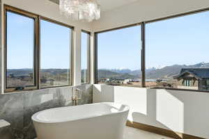 Full bath with a mountain view, a soaking tub, a chandelier, and tile walls