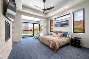 Carpeted bedroom featuring access to exterior, recessed lighting, a raised ceiling, a ceiling fan, and a fireplace