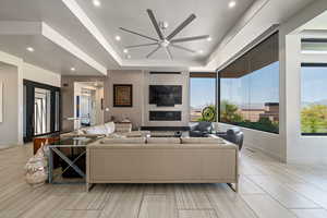 Living room with a ceiling fan, a tray ceiling, recessed lighting, and a large fireplace