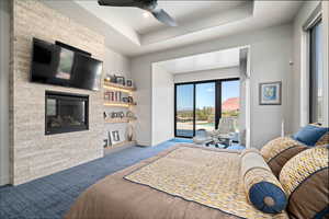 Bedroom featuring access to exterior, carpet flooring, a fireplace, a tray ceiling, and a ceiling fan