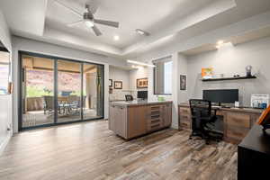 Office featuring a raised ceiling, light wood finished floors, ceiling fan, and recessed lighting