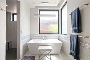 Bathroom featuring tile walls, plenty of natural light, a freestanding tub, tile patterned floors, and wainscoting