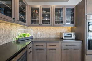 Bar area with decorative backsplash, stainless steel double oven, and wine cooler