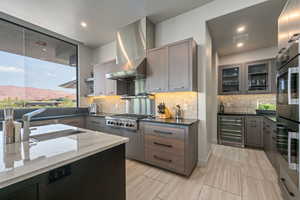 Kitchen featuring wine cooler, appliances with stainless steel finishes, dark stone countertops, extractor fan, and decorative backsplash