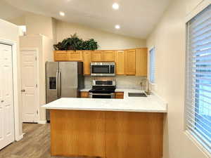 Kitchen with a peninsula, vaulted ceiling, stainless steel appliances, light wood finished floors, and recessed lighting