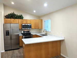 Kitchen featuring stainless steel appliances, a peninsula, dark wood-type flooring, vaulted ceiling, and light stone countertops