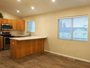 Kitchen featuring appliances with stainless steel finishes, a peninsula, light countertops, dark wood-style floors, and recessed lighting
