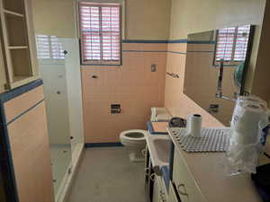 Full bath with tile walls, a walk in shower, healthy amount of natural light, tile patterned floors, and vanity