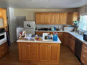 Kitchen featuring white appliances, wood finished floors, light countertops, a kitchen island, and brown cabinetry