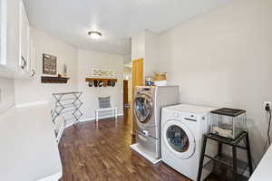 Laundry area featuring cabinet space, washing machine and dryer, dark wood-style flooring, and a textured ceiling
