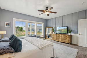 Carpeted bedroom featuring ceiling fan and a decorative wall