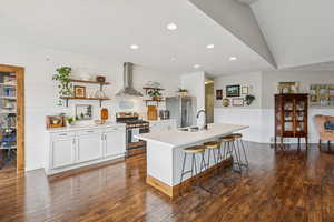 Kitchen with stainless steel appliances, light countertops, wall chimney exhaust hood, open shelves, and white cabinetry
