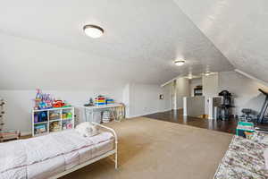 Bedroom with a textured ceiling, vaulted ceiling, and carpet