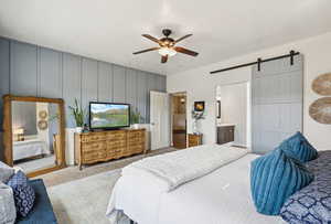 Bedroom with a barn door, carpet, ensuite bathroom, and ceiling fan