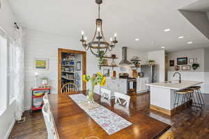 Dining space with a chandelier, dark wood-style flooring, recessed lighting, and wood walls