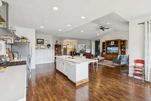 Kitchen with stainless steel range with gas stovetop, ceiling fan, dark wood-type flooring, open floor plan, and vaulted ceiling
