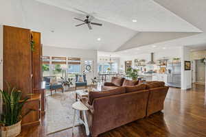 Living room featuring dark wood finished floors, lofted ceiling, a ceiling fan, a chandelier, and a textured ceiling