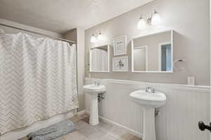 Full bath featuring tile patterned floors, a wainscoted wall, a textured ceiling, and shower / bath combo with shower curtain