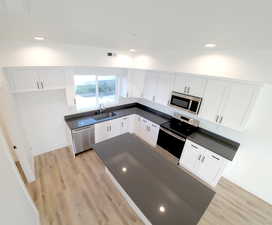 Kitchen featuring stainless steel appliances, dark countertops, light wood-style floors, white cabinetry, and recessed lighting