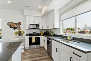 Kitchen featuring appliances with stainless steel finishes, dark countertops, white cabinetry, recessed lighting, and wood finished floors