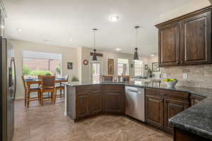 Kitchen featuring dark brown cabinets, stainless steel appliances, decorative backsplash, dark stone counters, and recessed lighting