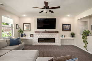 Living room with carpet, a ceiling fan, and a glass covered fireplace