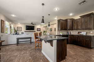 Kitchen with a kitchen breakfast bar, open floor plan, dark brown cabinetry, a ceiling fan, and dark marble finish flooring