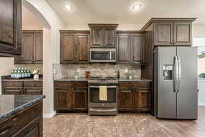 Kitchen featuring stainless steel appliances, dark brown cabinetry, arched walkways, backsplash, and recessed lighting