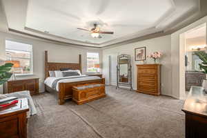 Bedroom featuring a tray ceiling, light carpet, ceiling fan, and ensuite bath