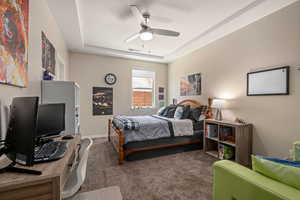 Carpeted bedroom featuring ceiling fan and a tray ceiling