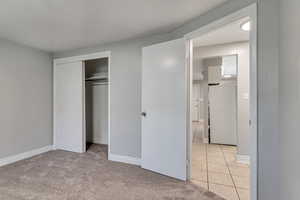 Unfurnished bedroom with a closet, fridge, light tile patterned flooring, and light carpet