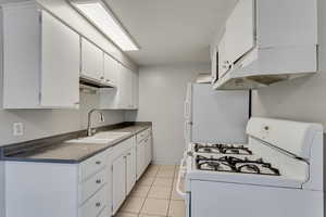Kitchen with white appliances, extractor fan, white cabinets, light tile patterned floors, and dark countertops