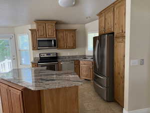 Kitchen featuring stainless steel appliances, stone counters, brown cabinetry, a center island, and light tile patterned floors