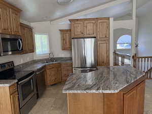 Kitchen with appliances with stainless steel finishes, vaulted ceiling, a kitchen island, stone countertops, and brown cabinets
