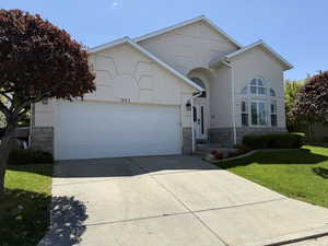 View of front facade featuring stone siding, a garage, stucco siding, a front lawn, and driveway