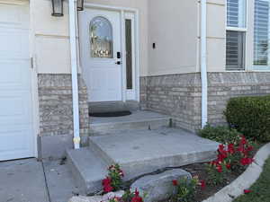 View of exterior entry featuring stone siding, a garage, and stucco siding